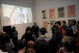 Personas escuchando presentación de mujer en exposición de afiches