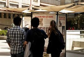 Grupo de personas observando la exposición itinerante "Montajes comunicacionales del pasado y del presente"